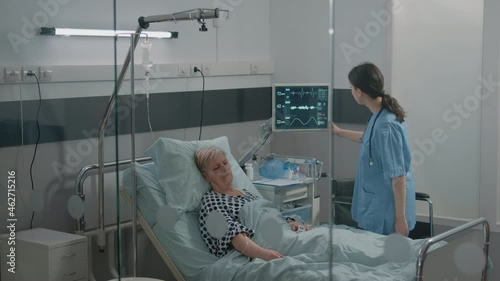 Medical assistant looking at heart rate monitor while patient sleeping in hospital ward bed. Nurse checking up on retired woman with nasal oxygen tube for healthcare and recovery. photo