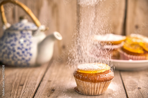 Sprinkling icing sugar on muffin with candied orange on top photo