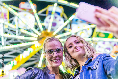 Portrait of mother and daughter taking selfie in front of big wheel at fair photo