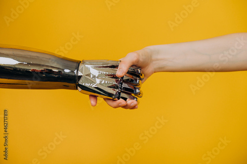 Injured person with stylish contemporary bionic prosthesis arm joins hands with young woman on yellow background close view