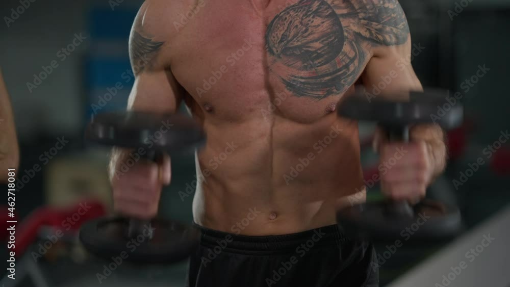 Front view muscular naked tattooed torso of Middle Eastern male bodybuilder lifting dumbbells. Unrecognizable motivated concentrated sportsman working out training in gym with equipment Front view muscular naked tattooed torso of Middle Eastern male bodybuilder lifting dumbbells. Unrecognizable motivated concentrated sportsman working out training in gym with equipment