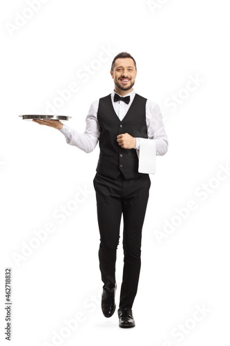 Full length portrait of a waiter carrying a silver tray and walking towards camera