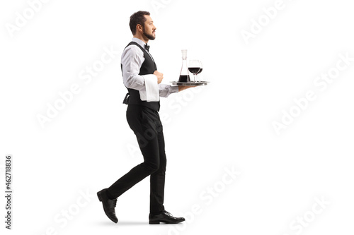 Photos Full length profile shot of a waiter carrying a red wine decanter on a silver tr