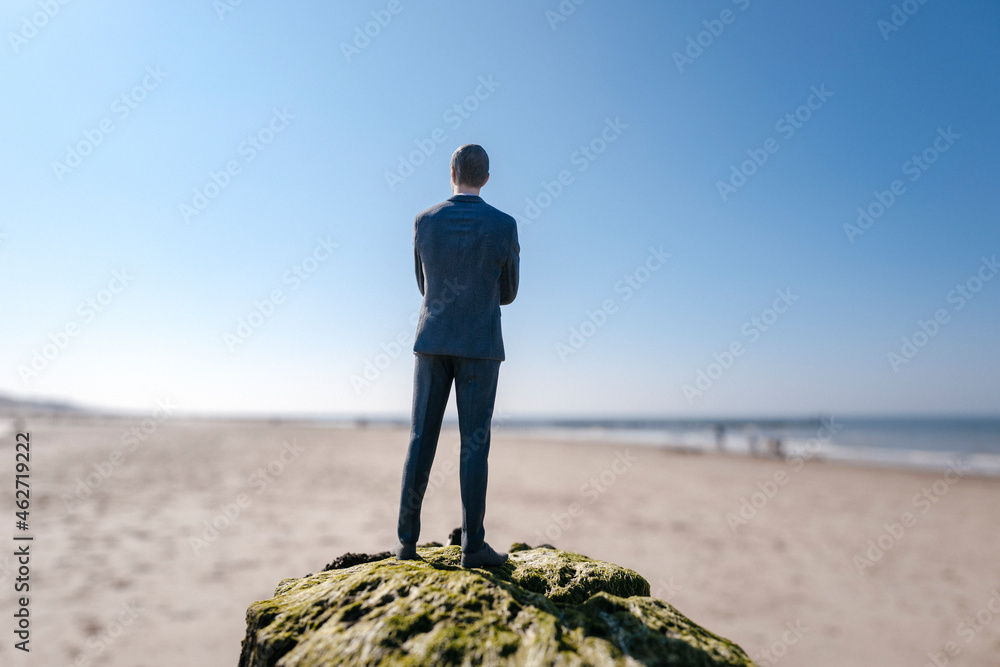 Businessman figurine standing on sand hill looking at view Businessman figurine standing on sand hill looking at view