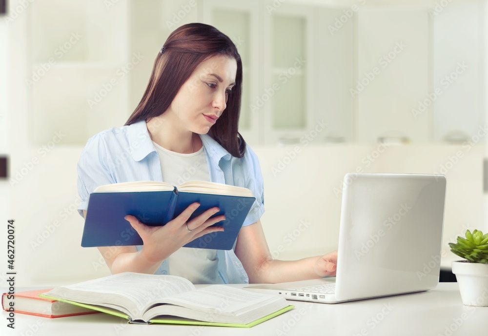 Caucasian female student working from home writing, sitting next to books Caucasian female student working from home writing, sitting next to books