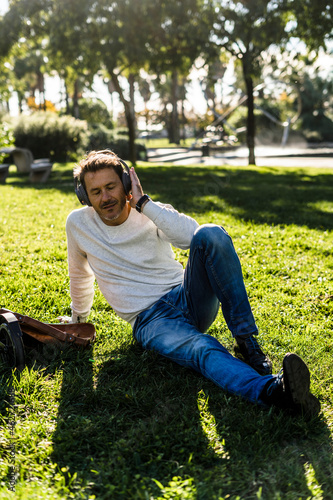 Casual businessman taking a break in a prak, sitting on grass, listening music photo