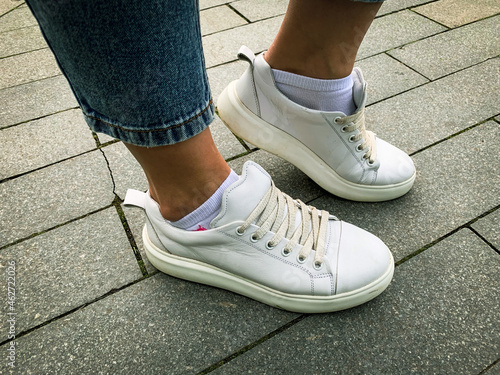 Woman legs wearing white leather laced sneakers outdoors, trendy shoes for urban life, walking in park