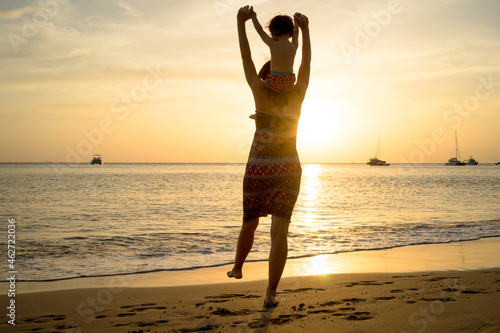 Thailand, Koh Lanta, back view of mother with baby girl on her shoulders at seashore during sunset photo