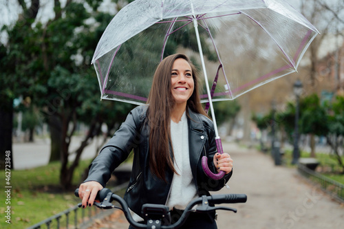 Smiling woman with electric bicycle holding umbrella at street in city