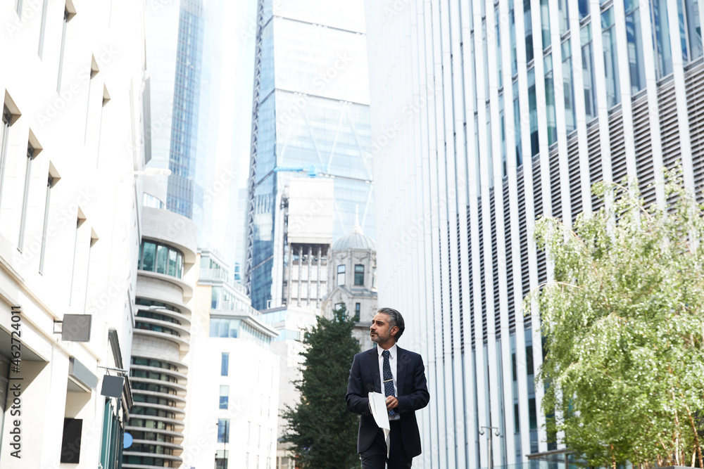 Entrepreneur with newspaper looking away while standing outside office in city Entrepreneur with newspaper looking away while standing outside office in city