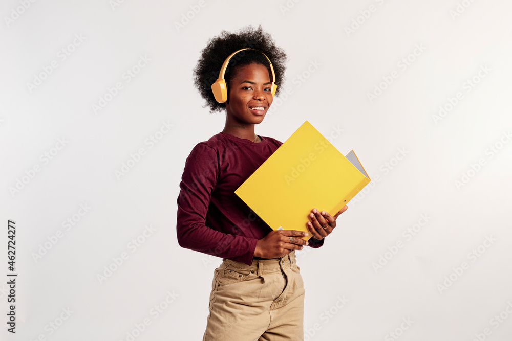 African American girl in brown sweater poses with her yellow folder while listening to music. African American girl in brown sweater poses with her yellow folder while listening to music.
