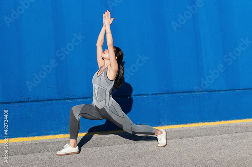 Woman doing Virabhadrasana by blue wall photo