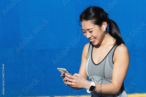 Smiling woman using mobile phone against blue wall photo