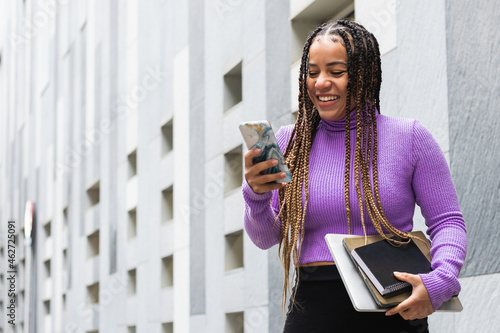 Smiling woman with books using smart phone while standing against gray wall photo