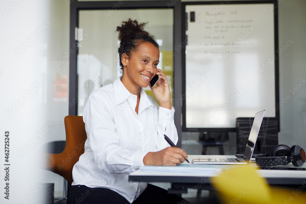 Portrait of smiling businesswoman on the phone sitting at desk in office Portrait of smiling businesswoman on the phone sitting at desk in office
