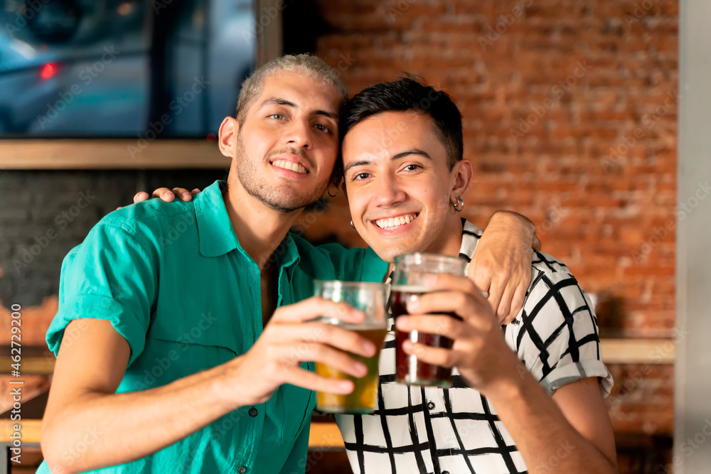 Happy gay couple with arm around holding beer glass at bar Happy gay couple with arm around holding beer glass at bar