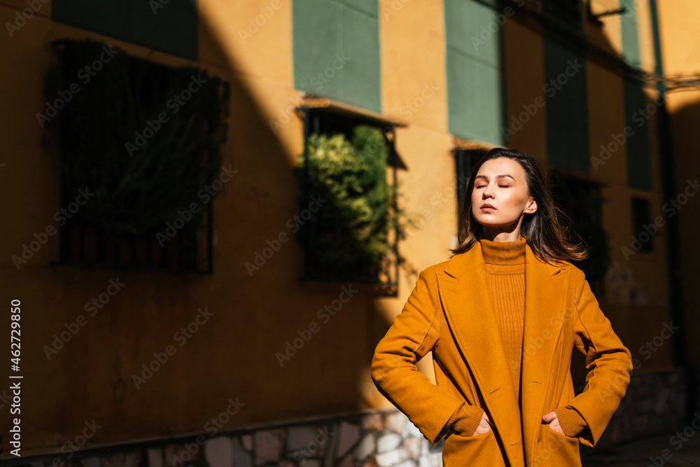 Young woman in winter coat standing with eyes by building Young woman in winter coat standing with eyes by building