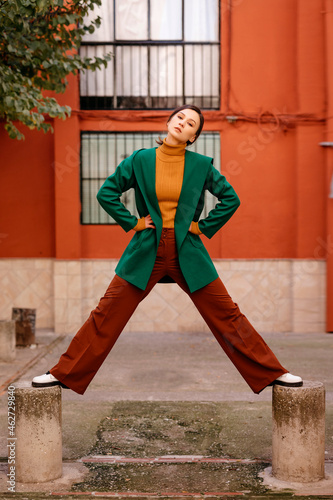 Young woman wearing green jacket standing on bollards against building in city