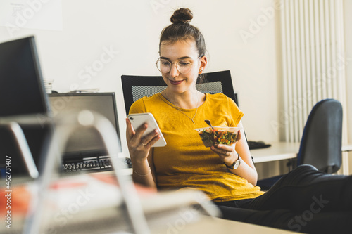 Smiling businesswoman using mobile phone during lunch break at office photo