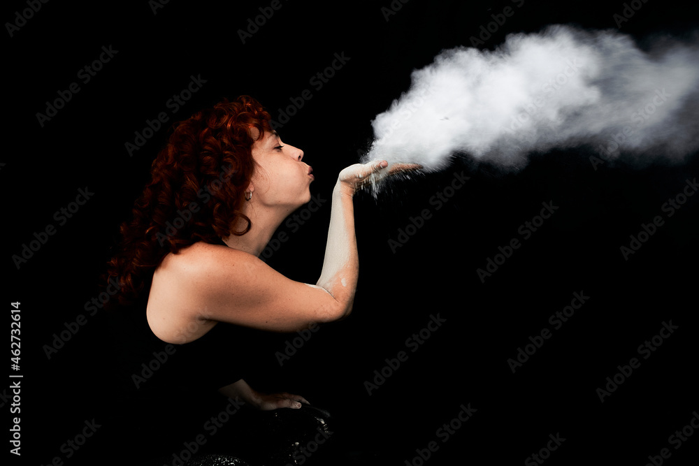 Woman blowing white dust while standing against black background Woman blowing white dust while standing against black background