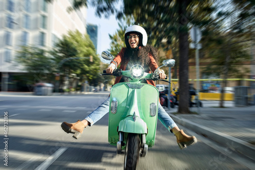 Cheerful woman riding motor scooter on street in city photo
