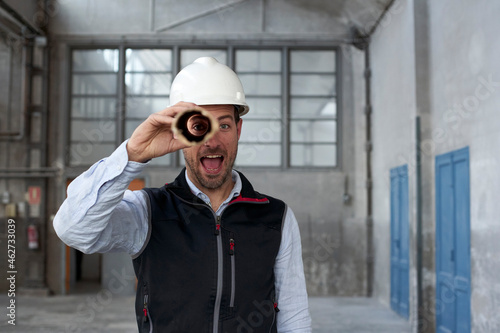 Male architect with mouth open looking through cardboard while standing in building photo