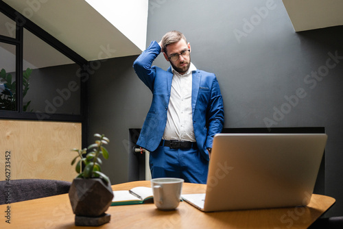 Confused businessman scratching head while looking at laptop on desk in creative office photo