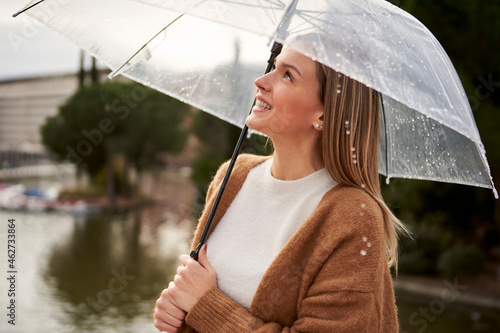 Happy woman looking up while holding umbrella during rainy season photo