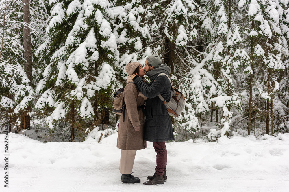 Young couple with backpack kissing while standing in forest Young couple with backpack kissing while standing in forest