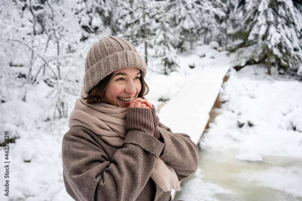 Happy woman wearing knit hat and jacket looking away while standing in forest Happy woman wearing knit hat and jacket looking away while standing in forest