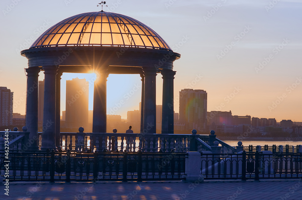 Rotunda with a transparent dome at sunset. Optical phenomena. Reflection, refraction, glare and halo. The figure of an unknown person from the back. Golden hour.
