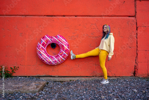 Young woman with dyed hair and floating tyre hanging on red wall photo