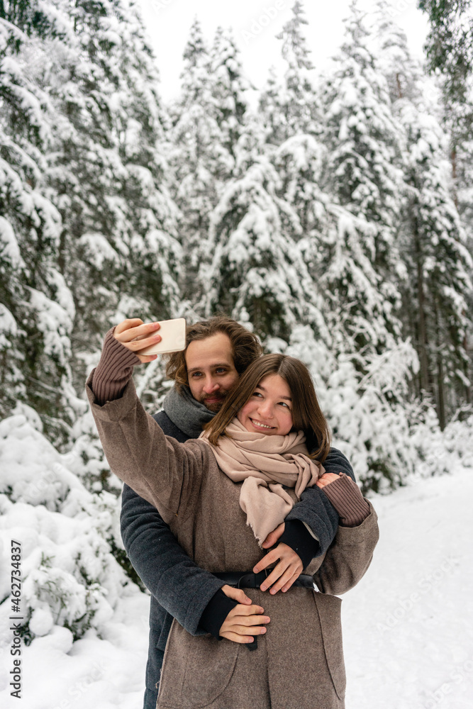 Girlfriend taking selfie through mobile phone with man embracing her from behind while standing at forest Girlfriend taking selfie through mobile phone with man embracing her from behind while standing at forest