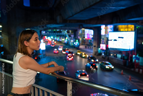 Young beautiful Asian woman walking down the street in the city looking traffic car on the road with illuminated night lights. Pretty girl enjoy urban outdoor activity lifestyle and city night life.