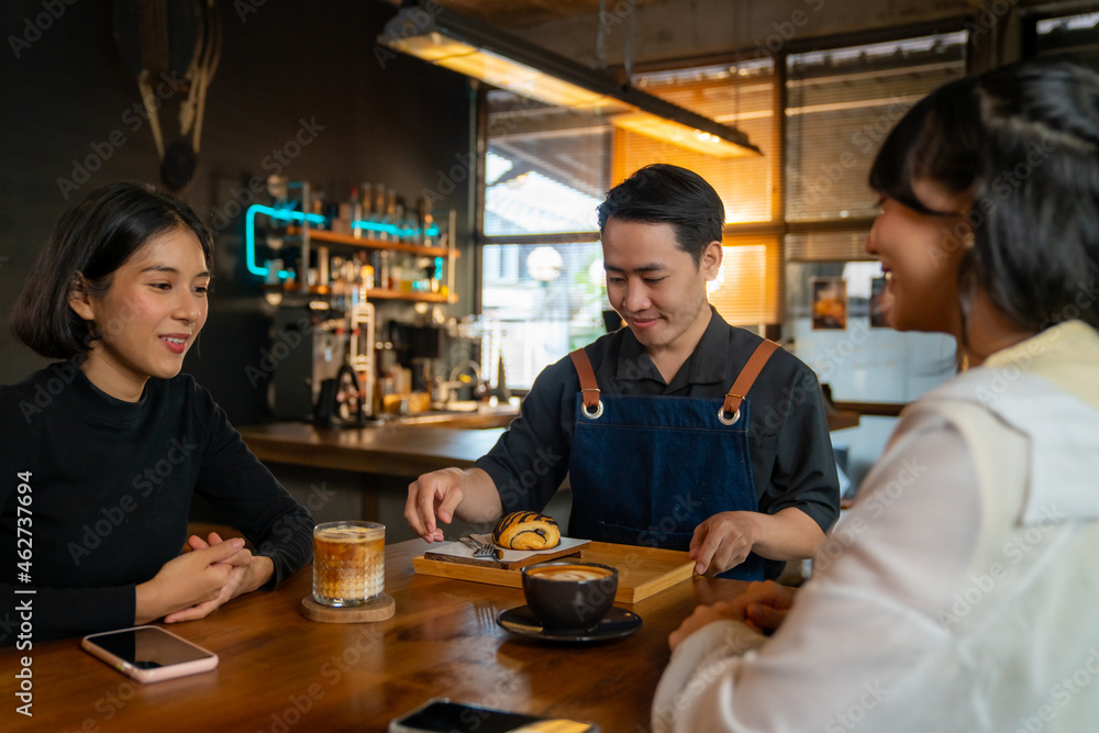 Asian man coffee shop waiter barista serving coffee latte and bakery to woman customer on the table at cafe. Attractive female friend meeting and talking together at restaurant. Small business concept