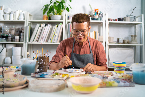 Asian LGBTQ guy learning color painting her self-made pottery at home. Confidence male enjoy hobbies and indoors leisure activity handicraft ceramic sculpture and painting workshop at pottery studio