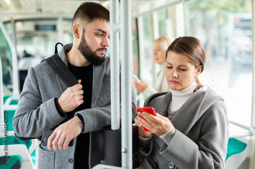 Attractive girl and bearded guy using mobile phones in city bus on way to work in fall day