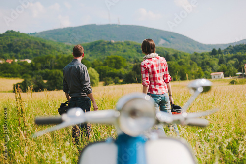 Back view of couple with vintage motor scooter standing on a meadow enjoying view, Tuscany, Italy photo