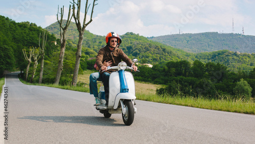 Couple riding vintage motor scooter on country road, Tuscany, Italy photo