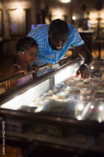 Afro father and his daughter looking at exhibits in glass stands at historical museum