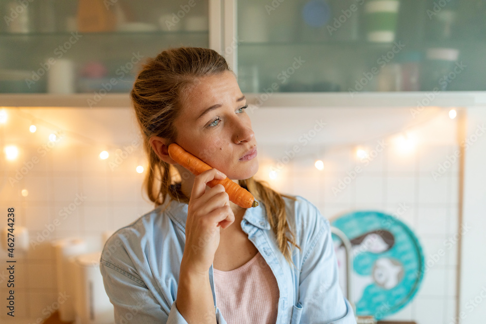 Young woman using carrot as a telephone at home Young woman using carrot as a telephone at home