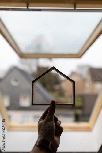 Hand holding wooden house model against window photo