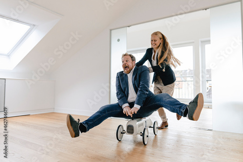 Playful businesswoman pushing businessman on toy car in office photo