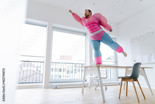 Businessman in office wearing pink bodybuilder costume pretending to fly photo