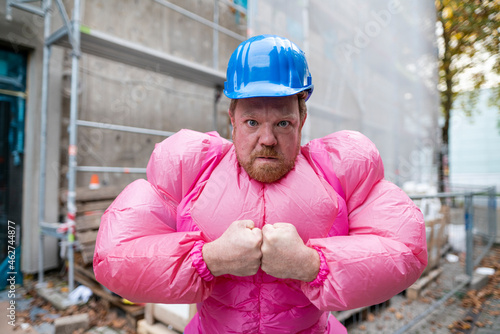 Portrait of man wearing pink bodybuilder costume and hard hat at construction site