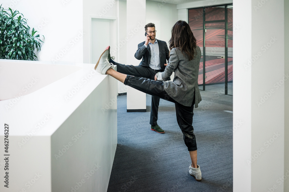 Businessman and woman standing on one leg in office