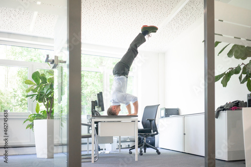 Businessman doing a headstand on desk in office