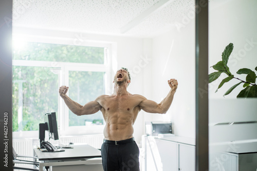 Screaming barechested businessman flexing muscles in office photo