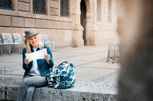 Smiling blond woman with baggage sitting on curb looking at map photo