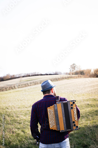 Back view of man with accordion on his shoulder on a meadow